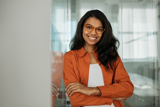 Woman with orange jacket smiling with arms folded