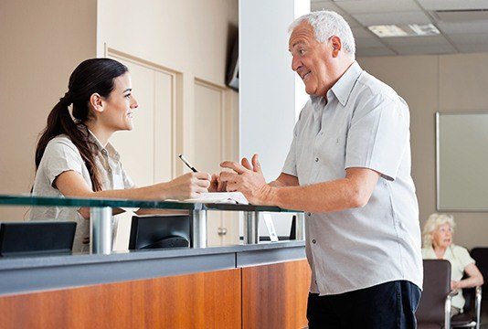 Man talking to team member at dental reception desk