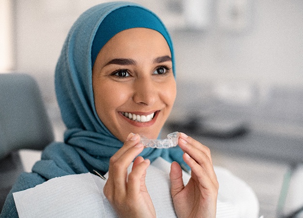Smiling woman holding clear aligner in dentist's office