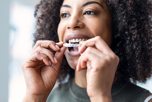 Smiling woman placing Invisalign aligner on top teeth