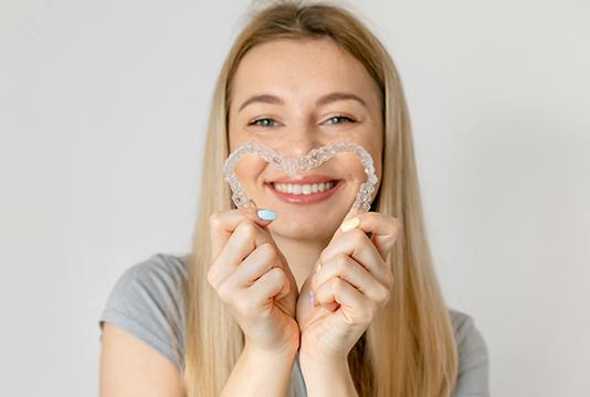Smiling woman creating heart-shape with clear aligners